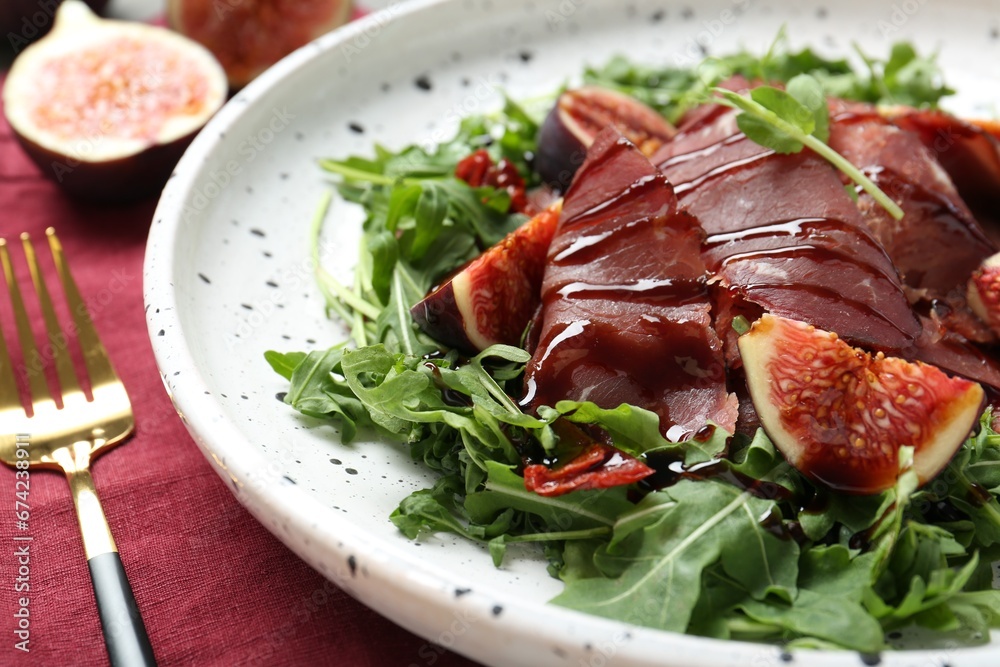 Plate of tasty bresaola salad with figs, sun-dried tomatoes, balsamic vinegar and fork on table, closeup