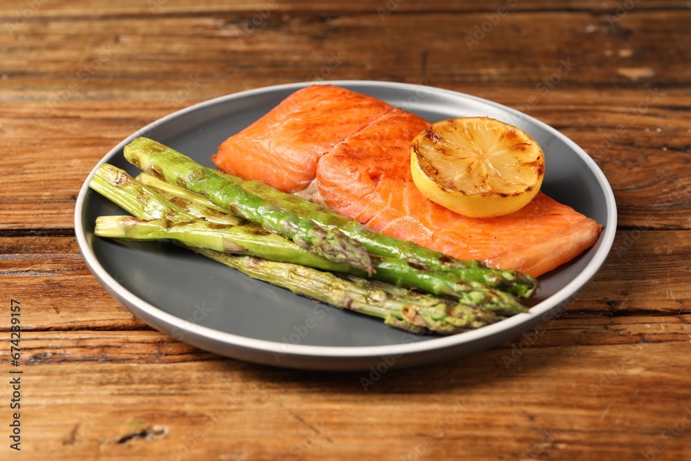 Tasty grilled salmon with asparagus and lemon on wooden table Tasty grilled salmon with asparagus and lemon on wooden table
