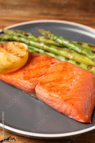 Tasty grilled salmon with asparagus and lemon on table, closeup