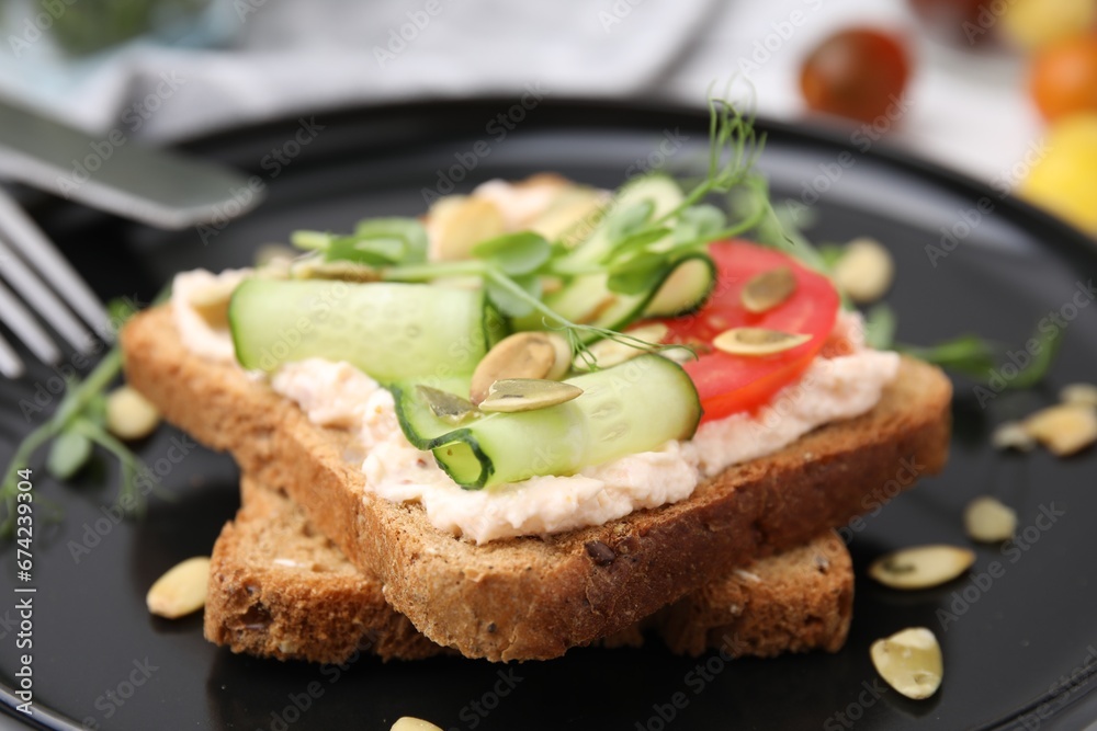 Tasty vegan sandwich with cucumber, tomato and pumpkin seeds on plate, closeup