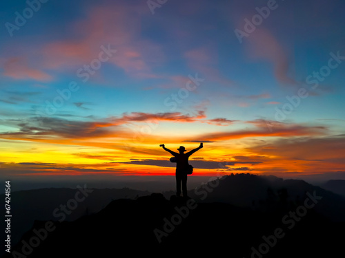 Silhouette backpack man standing on top of Mountain at sunset with vivid clouds.A man stands and takes a selfie against a scene with a red sky.