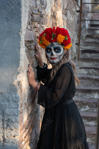 Young woman with painted skull on her face for Mexico's Day of the Dead (El Dia de Muertos) against color background