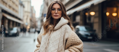 A girl with a European background is strolling by the street wearing a large down jacket in beige a sweater made from knitted fabric flared jeans and carrying a handbag She also has glasses