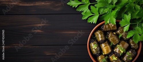 A flat lay image showcases a dolma a typical Middle Eastern dish with stuffed grape leaves and parsley placed on a black plate set against a dark wood background providing a panoramic view  photo