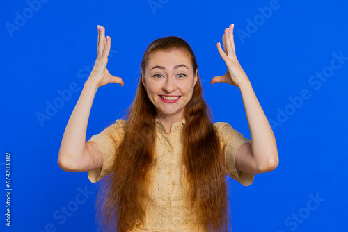 Excited amazed woman touching head and showing explosion, looking worried and shocked, celebrating success idea. Looking surprised of win wow redhead adult girl isolated on blue studio background