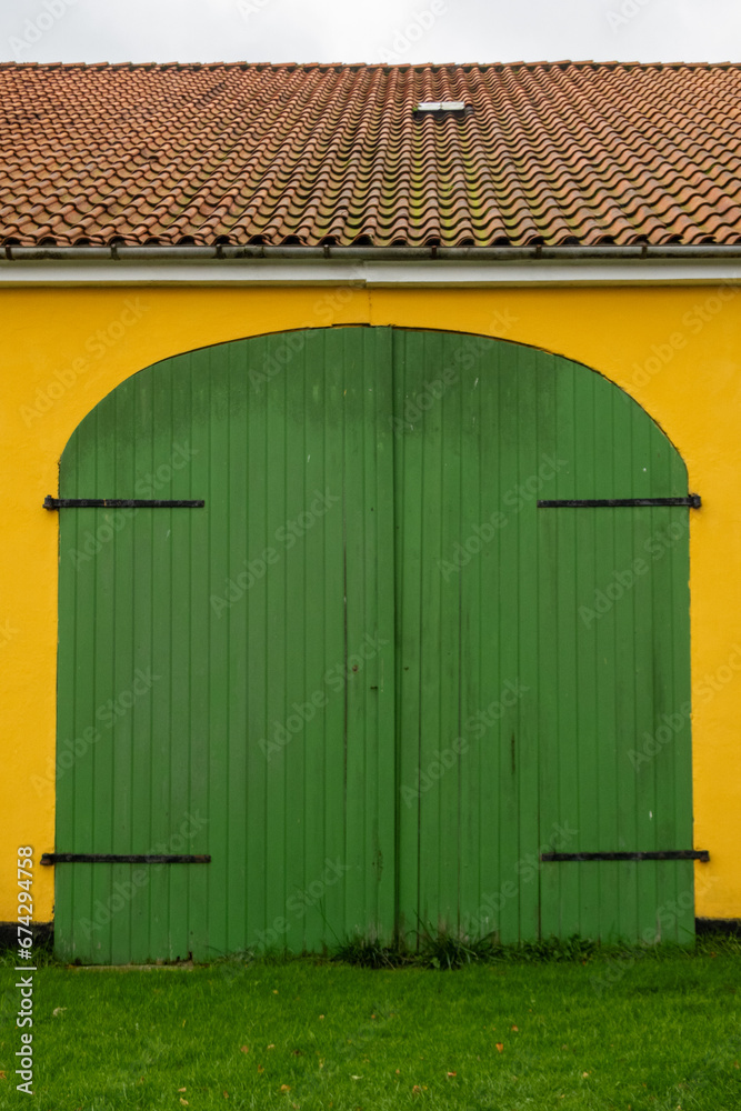 Sonder Bjert, Denmark A green wooden door with black hinges on an orange barn Sonder Bjert, Denmark A green wooden door with black hinges on an orange barn