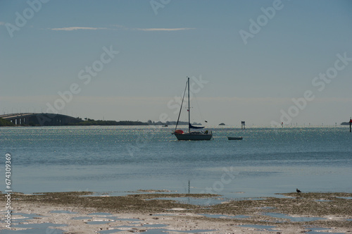 Maximo Beach Park bay water in St. Petersburg, FL. Sailboat no mast with a birds in water in front of the boat.. Looking south from the beach with sand, birds and water reflections. Sunny blue sky w