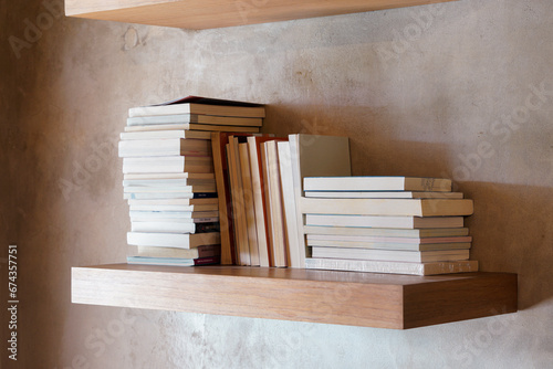 Stack of books on floating wooden bookshelf. Education and knowledge concept. Pile of books to read. House interior decoration
