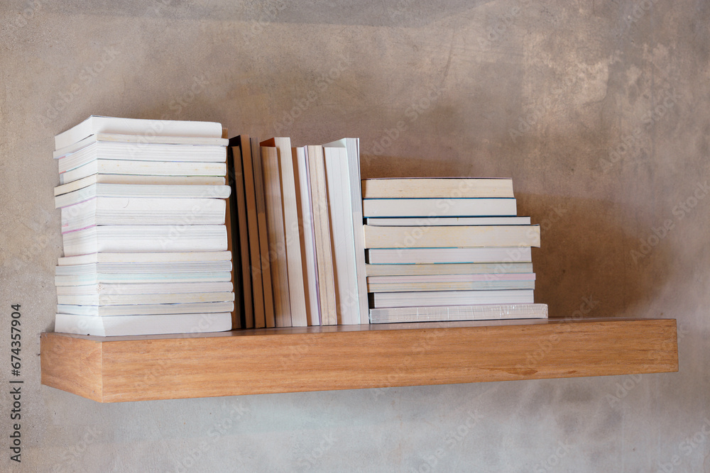 Stack of books on floating wooden bookshelf. Education and knowledge concept. Pile of books to read. House interior decoration Stack of books on floating wooden bookshelf. Education and knowledge concept. Pile of books to read. House interior decoration
