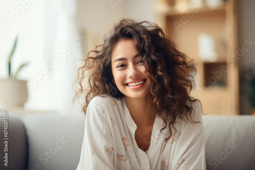 Woman sitting on couch, looking directly at camera with smile. This image can be used to convey happiness and positivity in various contexts.