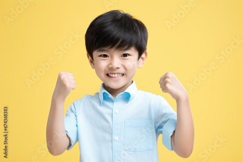 Young boy in blue shirt raising his fists. Perfect for showing strength and determination. Ideal for sports, empowerment, and motivation-themed projects.