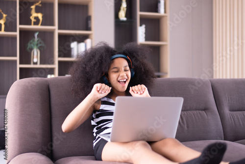 Fototapeta Naklejka Na Ścianę i Meble -  Happy young african girl listening to music on laptop and internet online