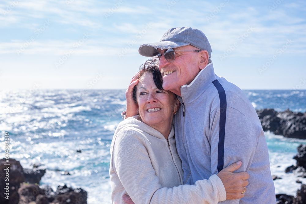 Caucasian senior couple embracing with love in vacation at sea enjoying a sunny day. Elderly smiling people in retirement expressing love and freedom