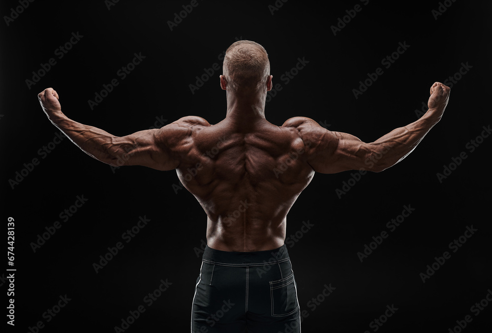 Naklejka premium Muscular man showing back muscles, isolated on black background. Strong male rear view