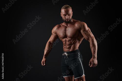 Muscular man shows his muscles against the background of a black wall. Bodybuilder, male naked torso, abs. © andy_gin