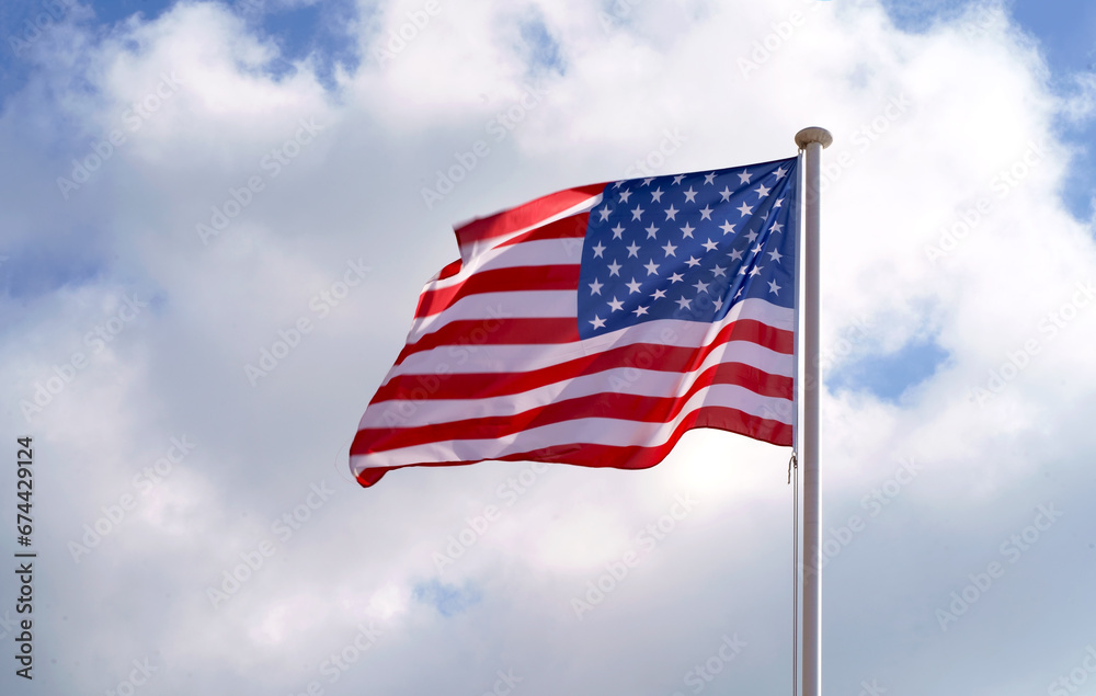 Large American flag waving on flag pole with cloud blue sky. Windy and sunny day with waving stars and striped flag