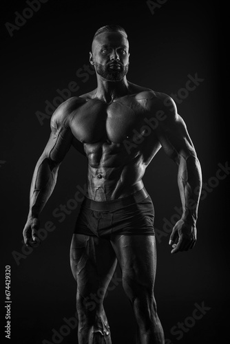 Silhouette of a strong bodybuilder. Confident young fitness athlete with a powerful body and perfect abs. Black and white photography. Dramatic light. © andy_gin