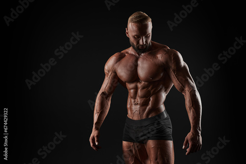 Muscular man shows his muscles against the background of a black wall. Bodybuilder, male naked torso, abs.
