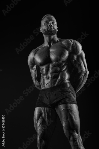 Silhouette of a strong bodybuilder. Confident young fitness athlete with a powerful body and perfect abs. Black and white photography. Dramatic light.