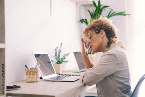 Tired woman touching neck and glasses in front of a. laptop in home office workplace. Small online business computer technology modern people concept lifestyle. Stress and problems notebook business photo