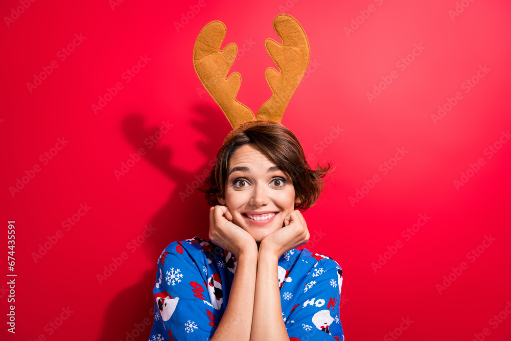 Portrait of adorable cheerful girl hands touch cheeks toothy smile deer horns headband isolated on red color background Portrait of adorable cheerful girl hands touch cheeks toothy smile deer horns headband isolated on red color background