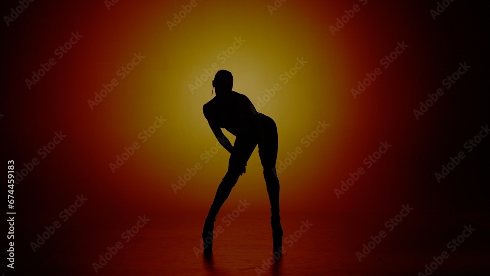 Woman dancer silhouette in high heels standing in the studio in yellow spotlight. Isolated on colorful background. Woman dancer silhouette in high heels standing in the studio in yellow spotlight. Isolated on colorful background.
