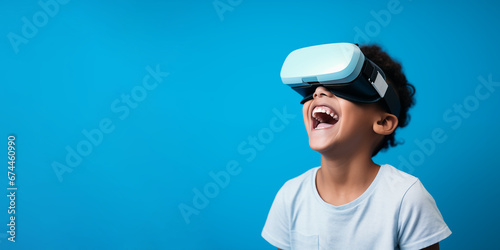 Young boy getting experience using VR headset glasses isolated on a blue background with copy space