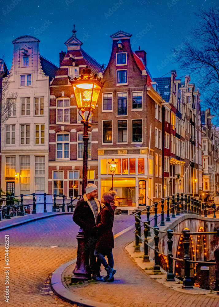 Fototapeta premium Amsterdam canals in the evening during Christmas, a couple of men and women on a city trip in Amsterdam in the Netherlands during winter. old city street with street lanterns in the evening