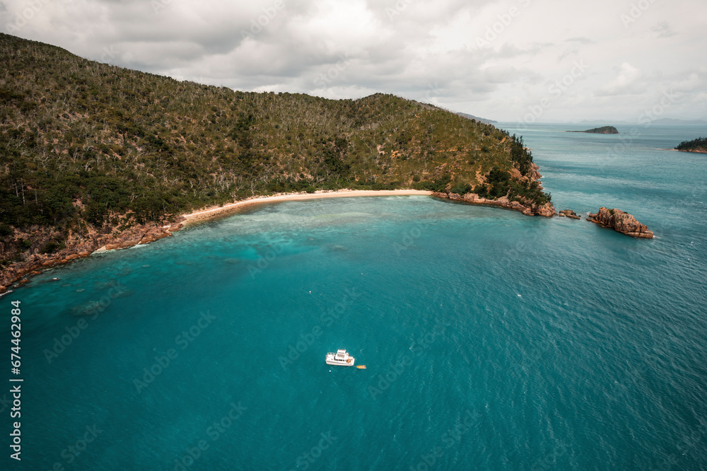 Aerial view of Blue Pearl Bay with a boat in the turquoise water and green hills behind the beach, Hayman Island, Australia. Aerial view of Blue Pearl Bay with a boat in the turquoise water and green hills behind the beach, Hayman Island, Australia.