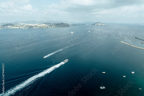 Aerial view of ferries and sailboats crossing the Gulf of Naples from Procida Island to Naples, view of Monte di Procida and Faro Capo Miseno promontory, Naples, Campania, Italy. photo