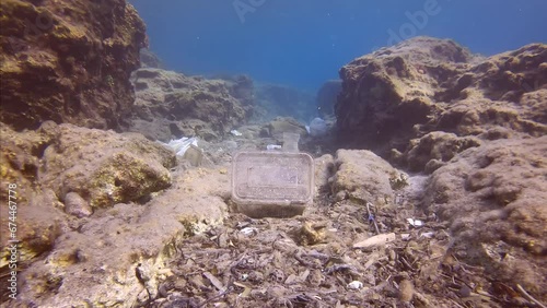 Seabed covered with wery many plastic garbage polluting Mediterranean Sea. Camera moving forwards low along seafloor covered with lots of plastic debris in crevice between cliffs.  photo