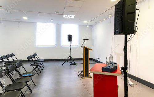 Modern and luminous room, empty, prepared for an event. Lectern with microphone and sound system and empty chairs to accommodate attendees