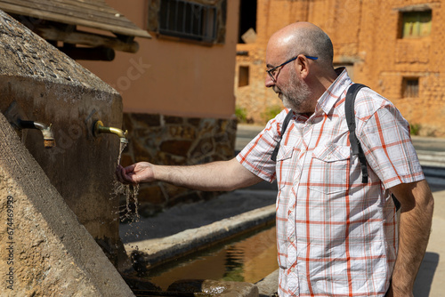adult man with beard collecting water with his hand from an old fountain in a village