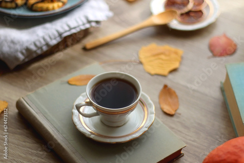 Cup of tea or coffee  plate with desserts  dried oranges  bowl of grapes  scented candles  vintage books  pumpkins and autumn leaves on the table. Autumnal hygge. Selective focus.