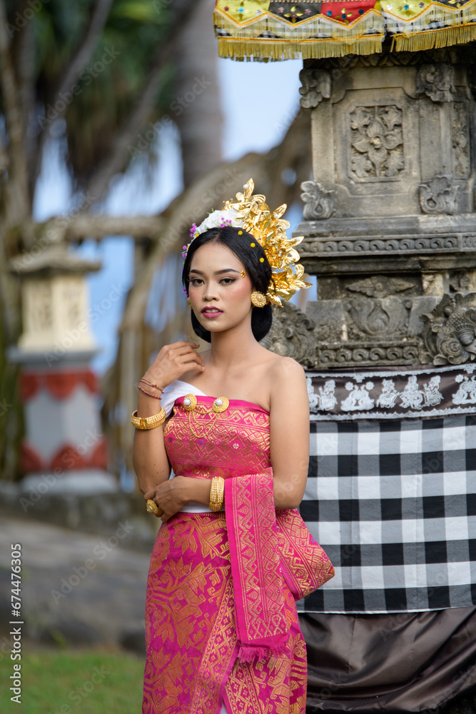 Balinese woman in vibrant traditional dress poses in front of a sacred temple