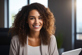 Woman with curly hair smiling at the camera with laptop.