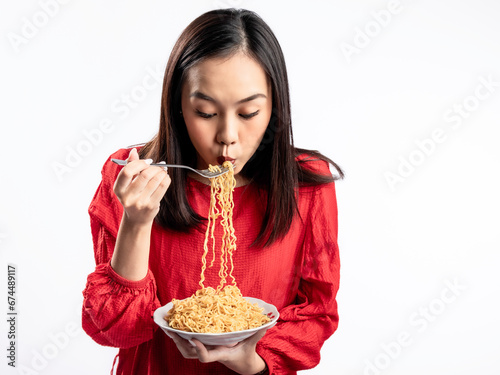 A portrait of a happy Asian woman wearing a red shirt  eating noodles. Isolated against a white background.