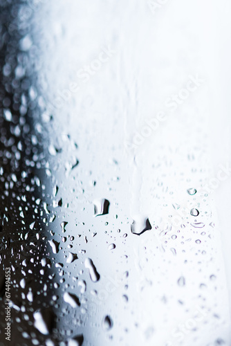 Plan serré d'une fenêtre avec gouttes d'eau de pluie en noir et blanc, mise au point sur une goutte, atmosphère mélancolique.