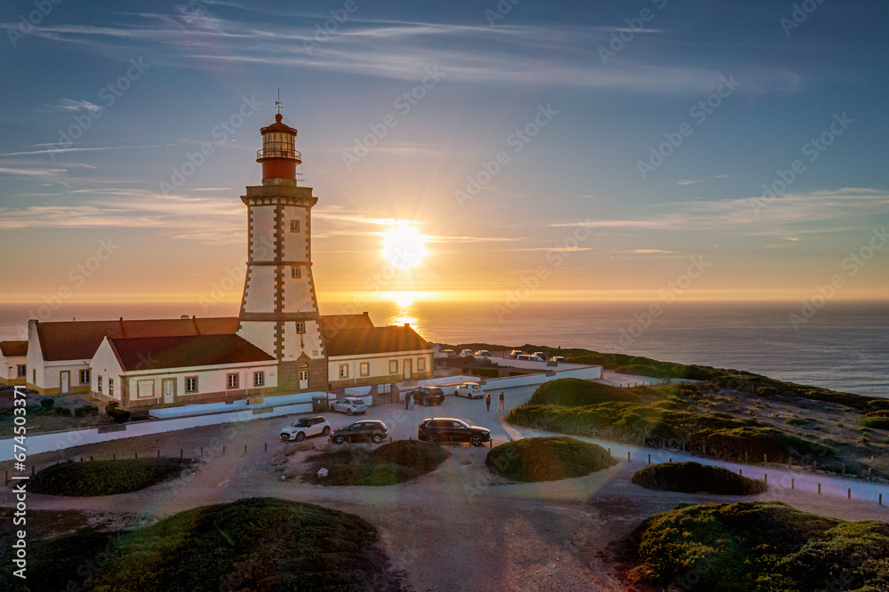 Portuguese lighthouse on cape Espichel at sunset, sea horizon and sun