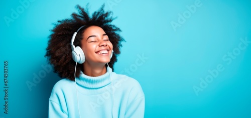 Young woman with afro hair smiling and listen music with headphones standing against a vibrant blue background. copy space for text