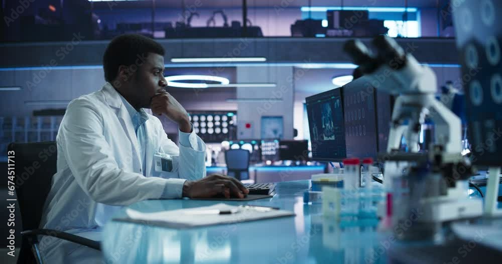 Black Male Neuroscientist Using Desktop Computer To Analyze MRI Scans Of Brain In Medical Research Center Laboratory. African American Surgeon Studying CT Scan Of Patient Suffering From Brain Tumor. Black Male Neuroscientist Using Desktop Computer To Analyze MRI Scans Of Brain In Medical Research Center Laboratory. African American Surgeon Studying CT Scan Of Patient Suffering From Brain Tumor.