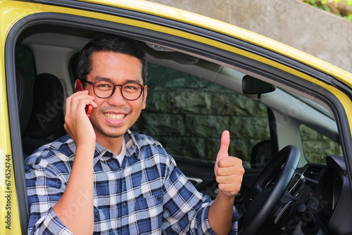 A man smiling and give thumb up while answering a phone call from inside his car photo