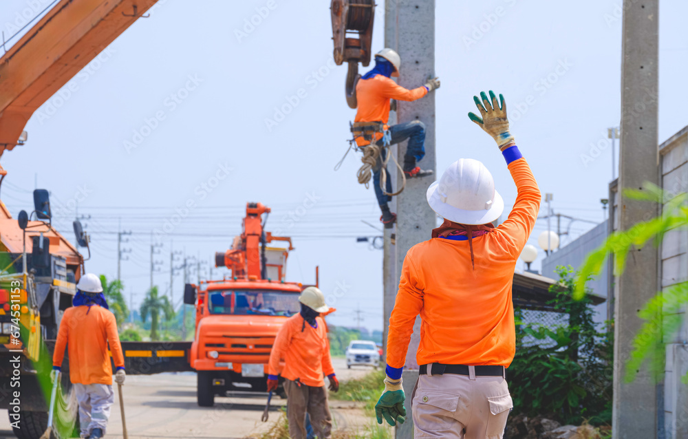 Group of electricians with cranes are installing new electrical pole on roadside area. One person is giving hand sign to give directions for the crane to work properly. Group of electricians with cranes are installing new electrical pole on roadside area. One person is giving hand sign to give directions for the crane to work properly.