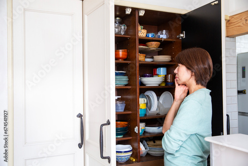 食器棚の収納に悩む女性、後ろ姿