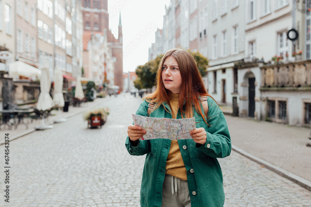 Portrait beautiful woman with paper map on urban street. Young worried female traveler lost in the city using map. Vacation concept by exploring interesting places to travel.