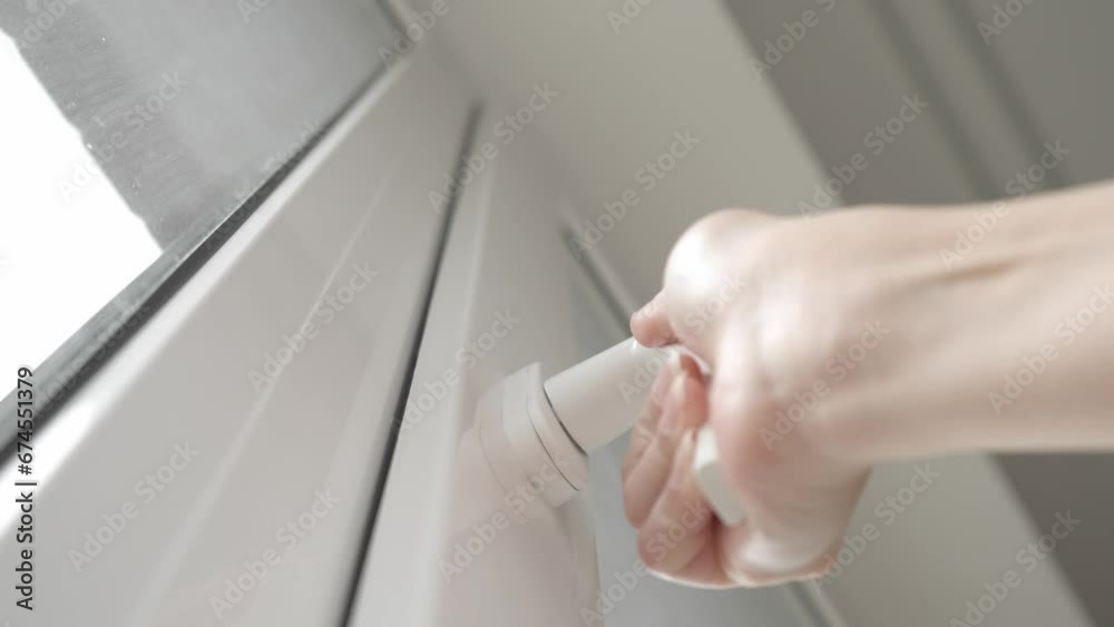 After airing the room, the woman closes the PVC plastic window and turns the handle of the locking mechanism to hermetically press the window frame sealer and keep the house warm.