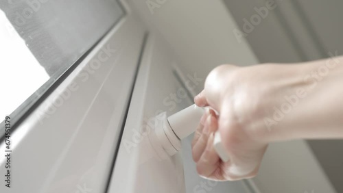 After airing the room, the woman closes the PVC plastic window and turns the handle of the locking mechanism to hermetically press the window frame sealer and keep the house warm.