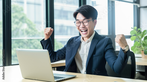 Happy successful asian business man investor wearing suit celebrating success in office looking at laptop rejoicing online investment financial win growth. 