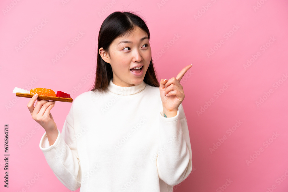 Young Chinese woman holding sashimi isolated on pink background intending to realizes the solution while lifting a finger up Young Chinese woman holding sashimi isolated on pink background intending to realizes the solution while lifting a finger up