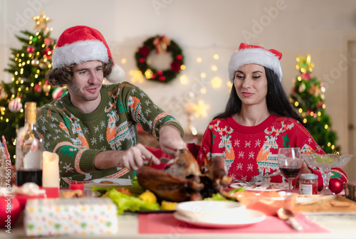 Young adult couple celebrating xmas Christmas thanksgiving in dining room with yummy roasted turkey happy together. People celebrate tradition christmastime holiday with delicious good taste chicken.